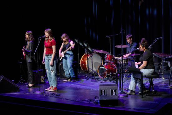 Teenage students sing and play electric guitar, drums and keyboard on stage at the Night of Music event in February 2024
